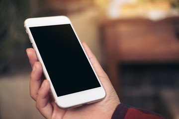 Mockup image of hand holding white mobile phone with blank black screen in cafe