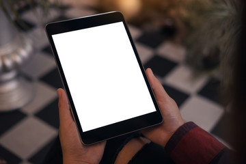 Top view mockup image of a woman sitting cross legged and holding black tablet pc with blank white desktop screen in cafe