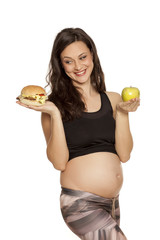 hungry pregnant woman has to choose between apple and hamburger on a white background