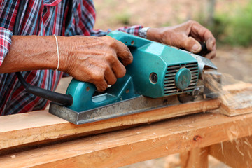 Hand of carpenter using electric planer with wooden plank smooth.