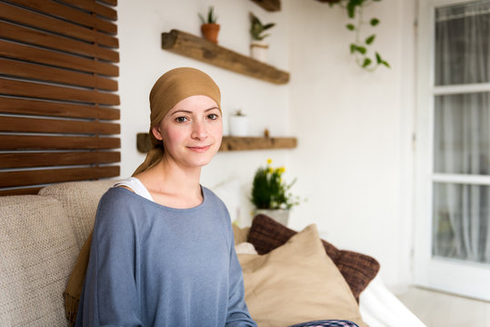 Portrait of young positive adult female cancer patient sitting in living room, smiling and looking at camera.