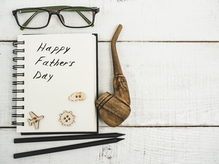 Smoking pipe and sketchbook with handwritten congratulation on Father's day on a beautiful, white table. Top view. Happy family concept