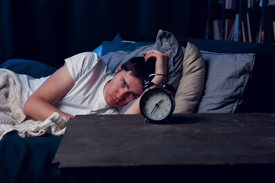 Image of brunet with insomnia lying in bed with alarm clock