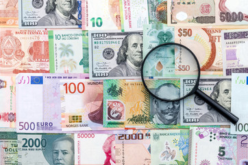 Magnifier on international money banknotes background, close up
