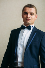 Handsome groom on a wedding day stand near the window