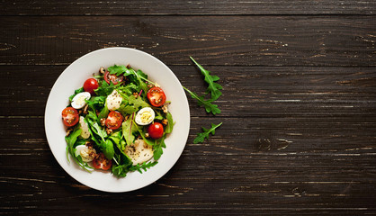 Fresh salad with tomatoes, mixed greens ,nuts, eggs, on wooden background . Healthy food.