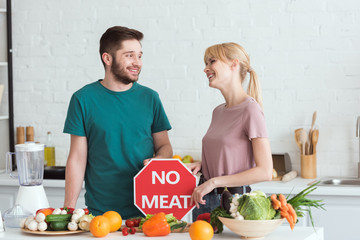 couple of vegans looking at each other with no meat sign in kitchen