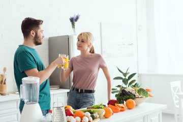 couple of vegans clinking with glasses of orange juice at kitchen