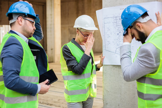 Team of successful young engineers and business partners facing problems during a meeting on a construction site. Looking at blueprints.