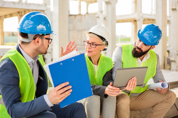 Team of successful young architects and business partners having a meeting on a construction site. Discussing project details