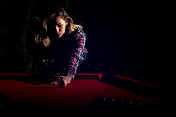 Young woman playing billiards in the dark billiard club