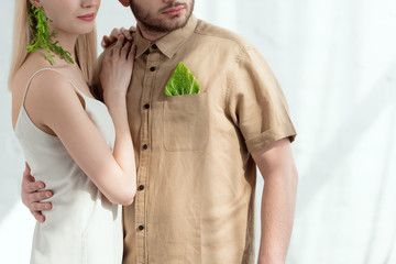 cropped shot of woman with earring made of arugula lean on boyfriend with savoy cabbage leaf in pocket, vegan lifestyle concept