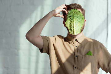 obscured view of pensive man with savoy cabbage leaf on face, vegan lifestyle concept