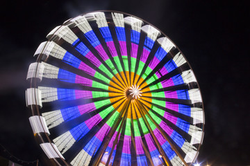 ferris wheels spinning with colorful lightpainting on a bavarian fair in germany at night, shot with long exposure