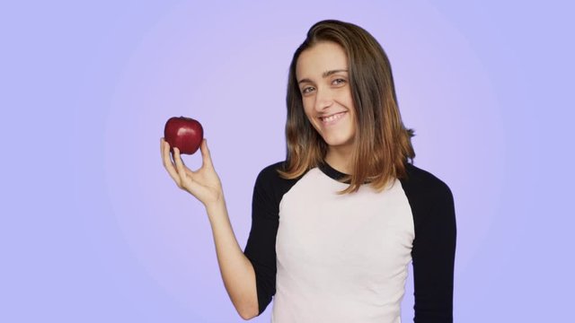 Pretty cute and beautiful young female with healthy lifestyle habits and eating organic biological food, holds fresh green apple, juicy and tasty fruit, smiles and chuckles flirt manner