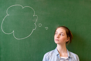 Student thinking blackboard concept. Pensive girl looking at thought bubble on chalkboard background. Caucasian student. Future, profession, possibilities concept.