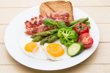 Fried eggs with bacon on the wooden table.