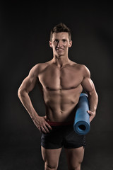 Fototapeta na wymiar Happy man hold yoga mat. Sportsman smile with sexy torso and six pack. Athlete smiling with strong arms in shorts. Gym equipment for training and workout. Sport yoga and fitness activity, vintage