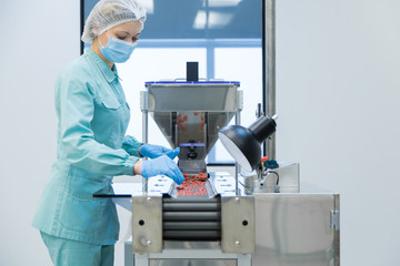 Pharmacy industry woman worker in protective clothing operating production of tablets in sterile...