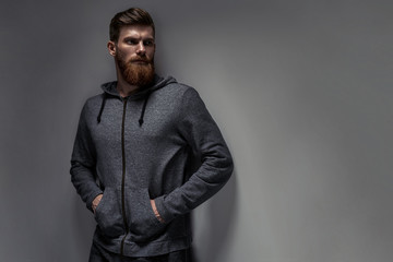 Obraz premium Portrait of handsome single bearded young man with serious expression in gray sportswear looking over gray background with copy space