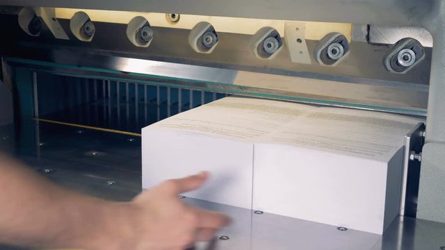Two long sheaves of paper are being cut in four by an industrial cutter