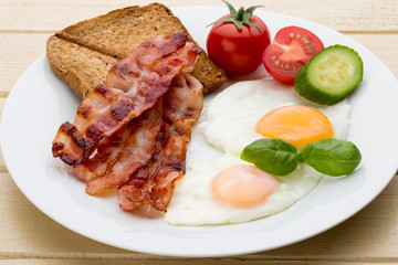Fried eggs with bacon on the wooden table.