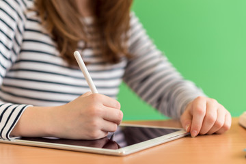 Young female student writing notes using digital tablet during class. Generation Z Education concept.