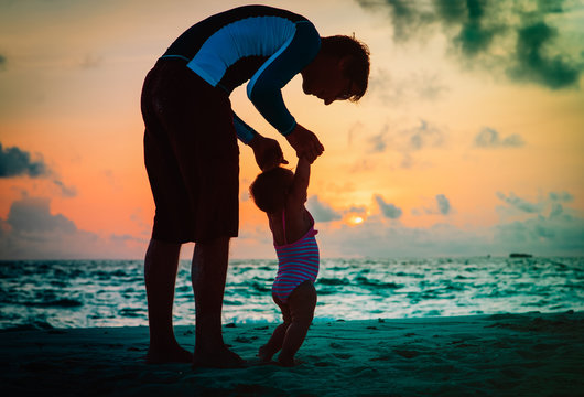 father and little daughter walk on sunset beach