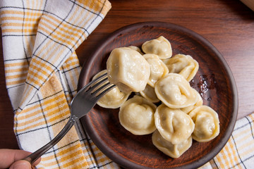 Close up view of boiled meat dumpling on metal fork. Served in clay plate Ukrainian meat dumplings or ravioli on wooden background..