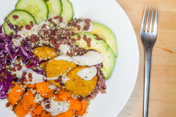 Vegan buddha bowl with Tempeh, Pumpkin, Red Cabbage, Cucumbers, Avocado and Hempseeds presented on a white plate