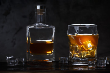 Alcohol in glass with ice and in bottle on dark background