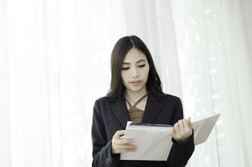 Asian women In black suit Standing holding a white book and smiling happily at work in the morning.Businesswoman standing White background,Black spots on the face of a woman caused by sunlight.