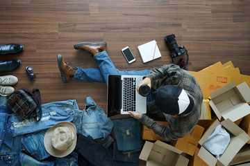 Top view of man holding coffee cup working laptop computer with fashion accessories on wooden floor...