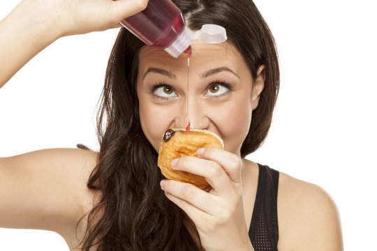 voracious young woman puts the topping on a donut on a white background