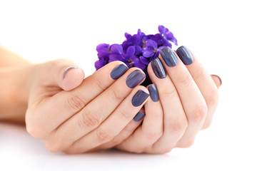 Hands of a woman with dark manicure on nails and bouquet of violets on a white background