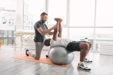 Rehabilitation training. Pleasant handsome man lying on the medball while lifting dumbbells