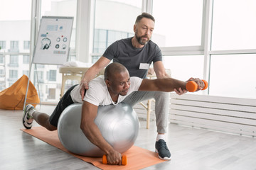 Rehabilitation exercises. Nice pleasant hard working man lying on the medball while having a workout
