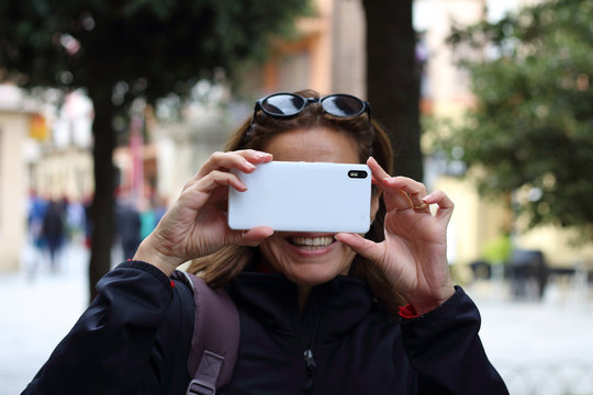 Retrato de una mujer sonriendo y sacando una fotograf&iacute;a con la c&aacute;mara del tel&eacute;fono m&oacute;vil 