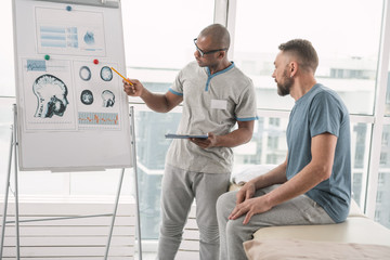 Obraz premium Medical explanation. Smart nice therapist pointing at the picture while explaining the diagnosis to the patient