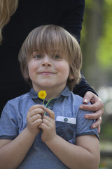 Niño sonriente (5 años), contento y feliz sujetando una flor en primavera. Se ve la mano de su madre abrazandole. © Aitor Diago