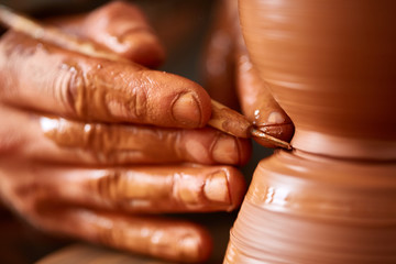Close-up hands of a male potter in apron making a vase from clay, selective focus