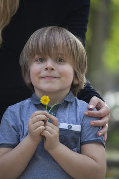 Ni&ntilde;o sonriente (5 a&ntilde;os), contento y feliz sujetando una flor en primavera. Se ve la mano de su madre abrazandole.