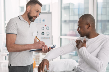 Description of symptoms. Pleasant young man talking to his doctor while describing symptoms