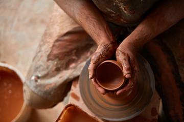 Close-up hands of a male potter in apron making a vase from clay, selective focus