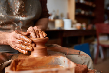 Close-up hands of a male potter in apron making a vase from clay, selective focus