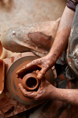 Close-up hands of a male potter in apron making a vase from clay, selective focus