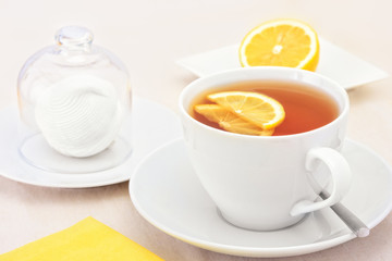 A cup of tea with lemon slices and zephyr, which is covered with a glass cap. Selective focus.
