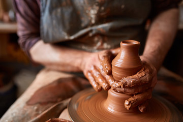 Close-up hands of a male potter in apron making a vase from clay, selective focus