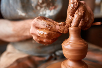 Close-up hands of a male potter in apron making a vase from clay, selective focus