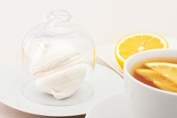 A cup of tea with lemon slices and zephyr, which is covered with a glass cap. Selective focus.
